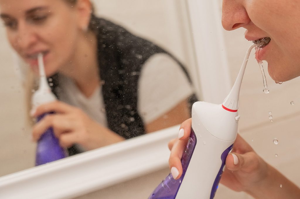 mujer lavándose los dientes con un irrigador dental