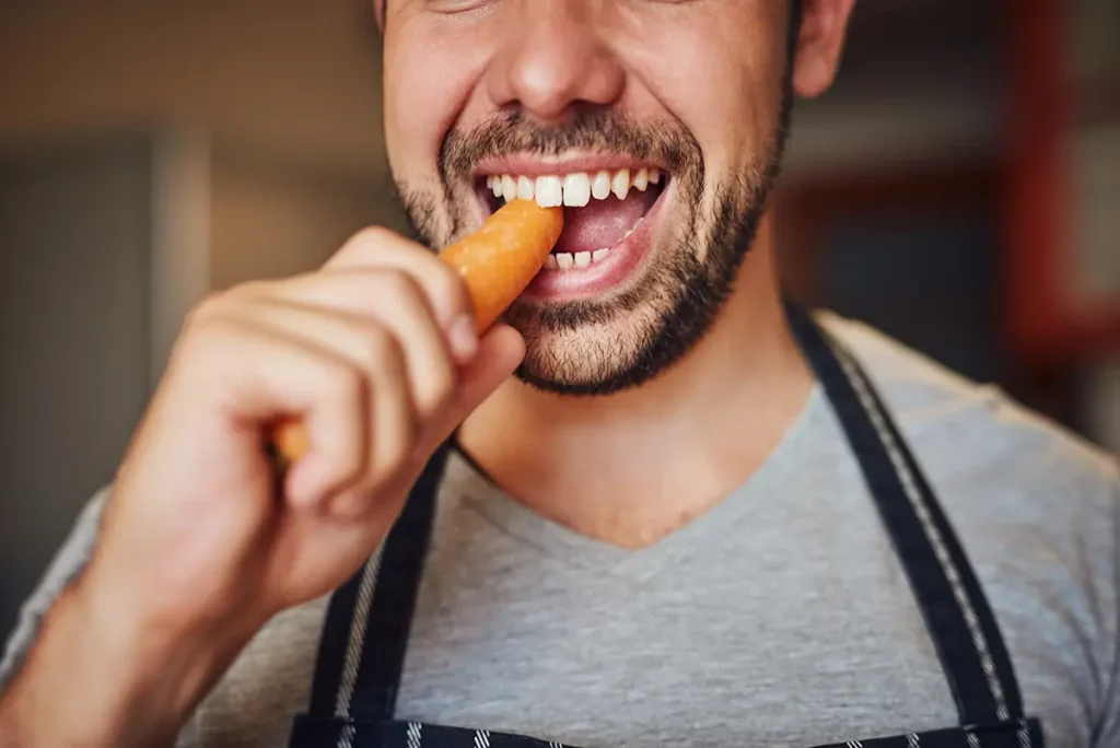 Hombre comiendo zanahoria para cuidar sus dientes en verano